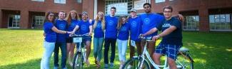 A group of undergraduate orientation leaders pose in matching blue shirts in front of dorms outside on the Biddeford Campus